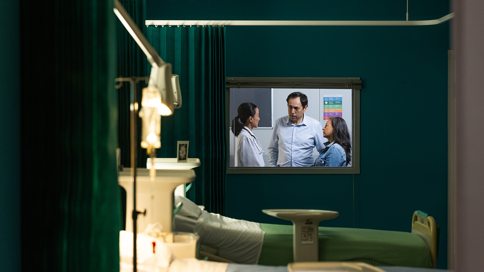 Chambre d'hôpital avec une famille vue à travers une fenêtre.
