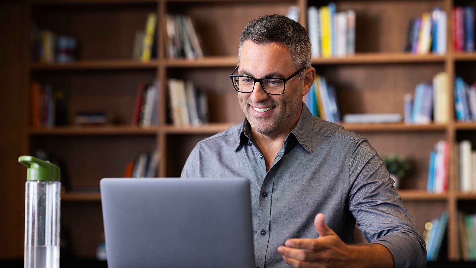 Un homme souriant utilise un ordinateur portable dans une bibliothèque.