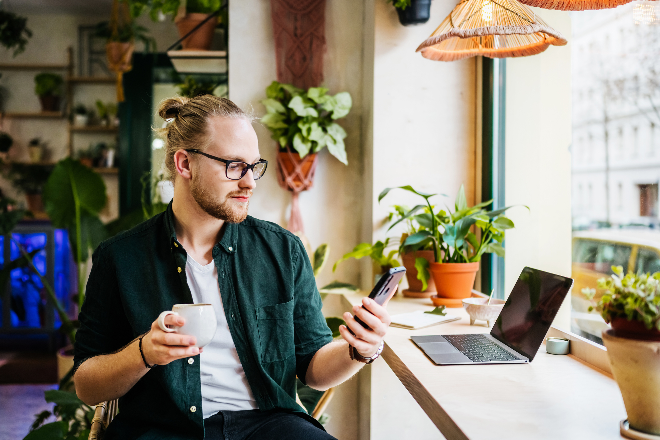 Un homme assis à un bureau à domicile devant un ordinateur portable, tenant un café.