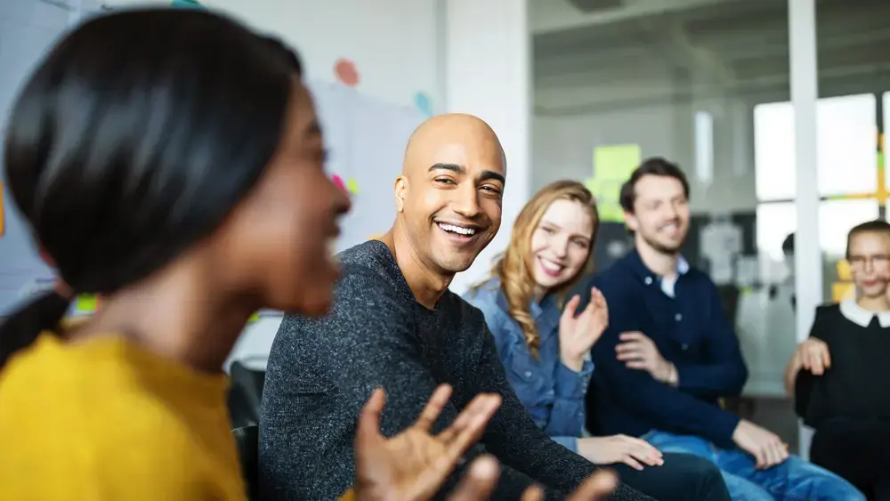 Un groupe de collègues assis, souriant et écoutant l'un d'entre eux parler.