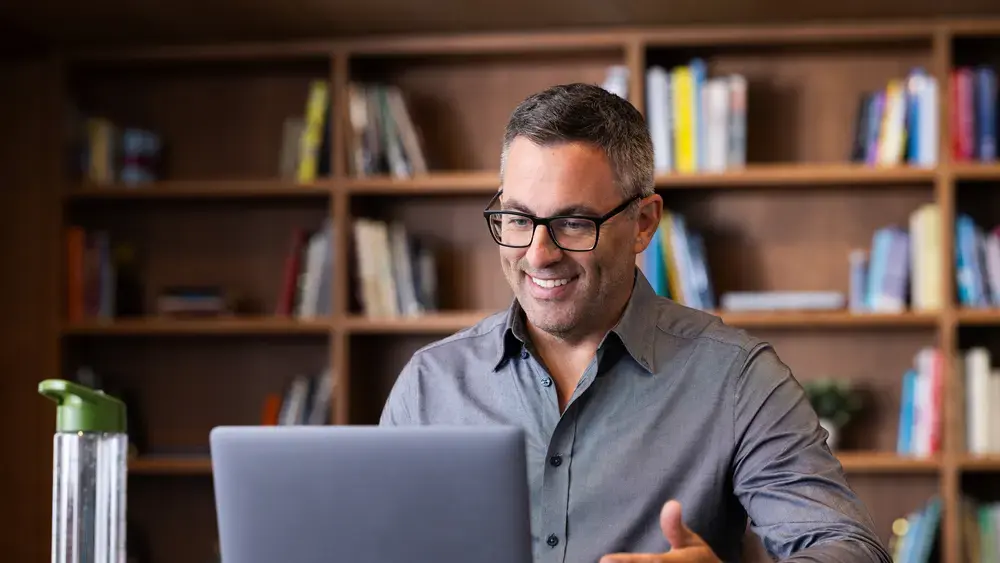 Un homme souriant utilise un ordinateur portable dans une bibliothèque.