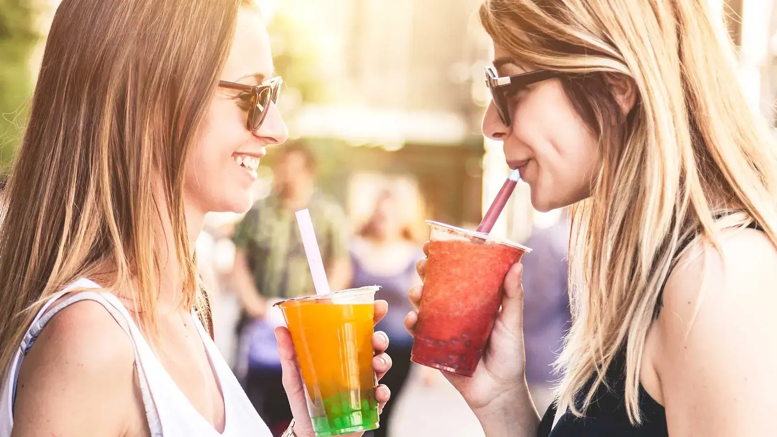 Deux femmes sourient en partageant des verres en plein air.