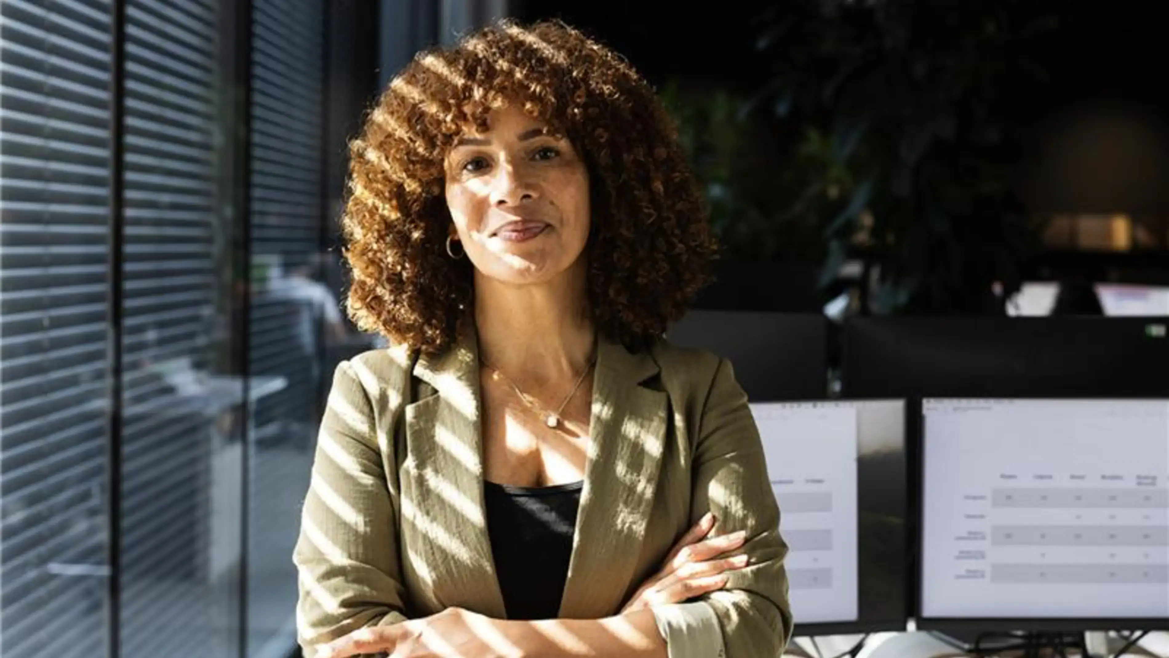 Une femme confiante, les bras croisés, près d'une fenêtre.