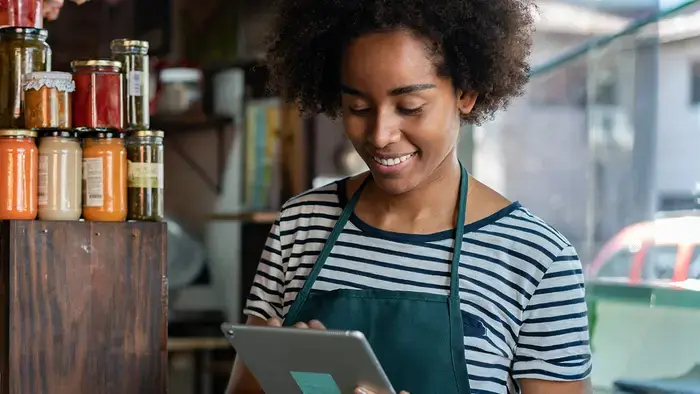 Une femme portant un tablier vert utilise une tablette à écran tactile dans un magasin.