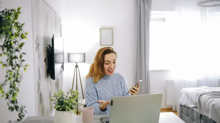 Femme en appel vidéo à la maison avec un ordinateur portable et un téléphone.