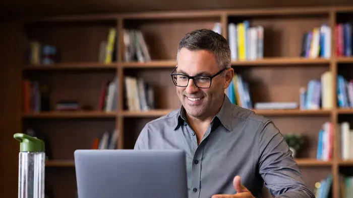 Un homme souriant utilise un ordinateur portable dans une bibliothèque.