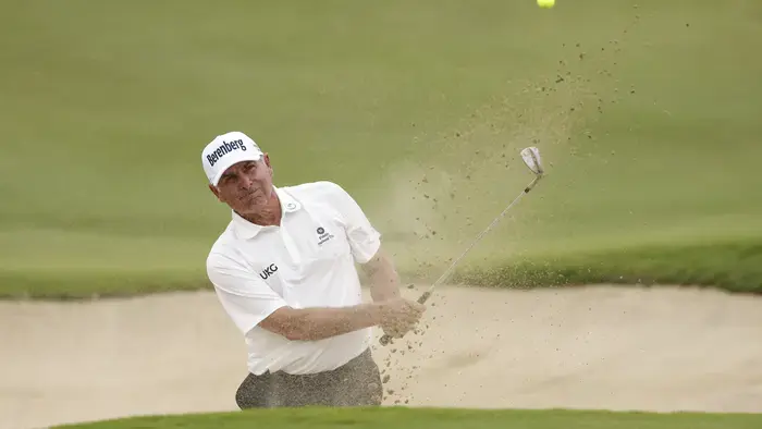Fred Couples sourit, vêtu d'une chemise à rayures rouges et blanches, sur un terrain de golf.