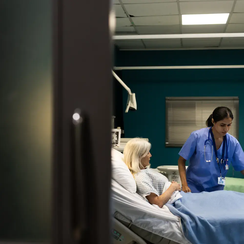 Une infirmière aide un patient âgé dans un lit d'hôpital.