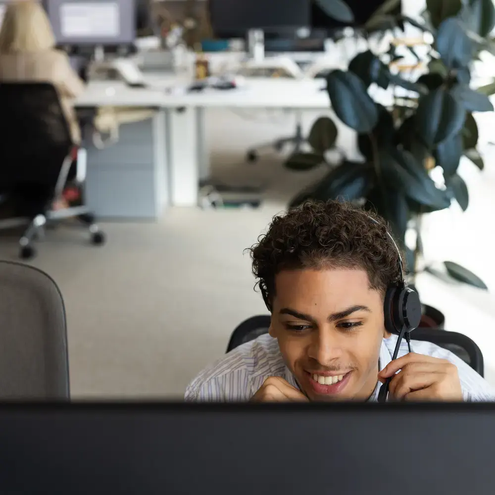 Personne souriante portant un casque devant un ordinateur.