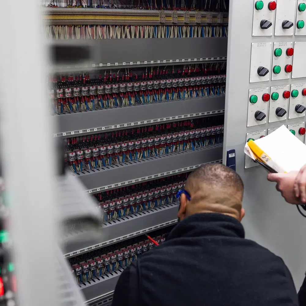 Deux techniciens inspectent des tableaux de commande électriques.