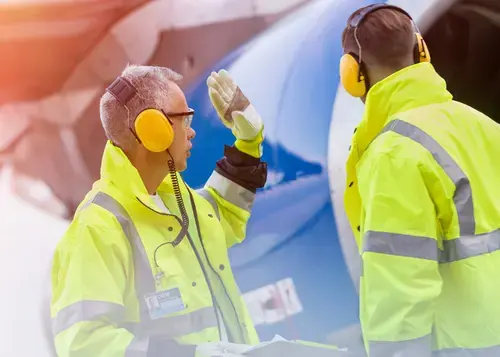 Deux travailleurs en veste jaune vif près d'un moteur d'avion.